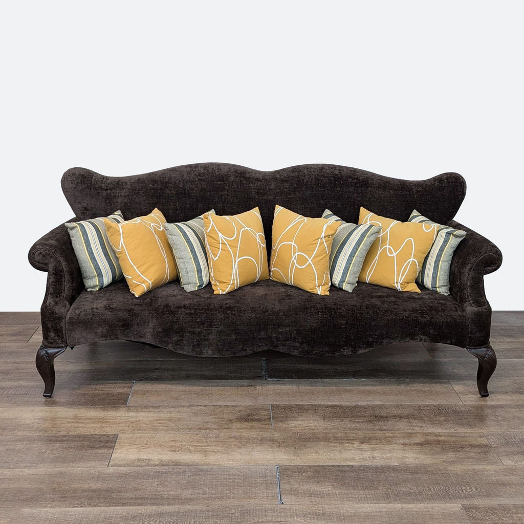 a brown velvet sofa with yellow and orange pillows.