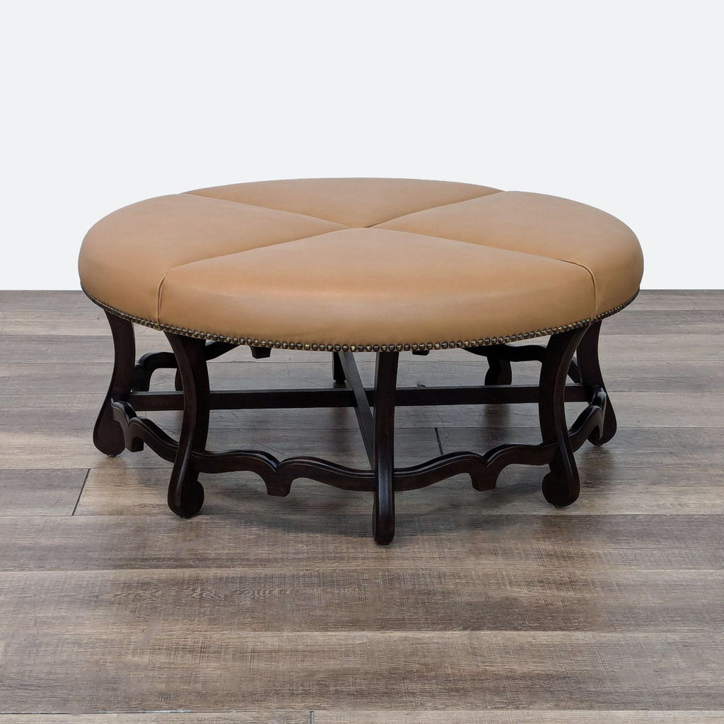 1. Round tan leather ottoman with a dark wood base, decorative nailhead trim, and elegant detailing by Reperch.