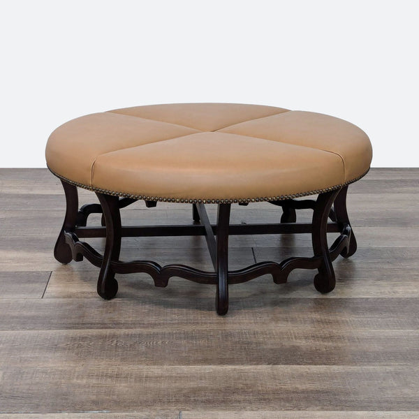 1. Round tan leather ottoman with a dark wood base, decorative nailhead trim, and elegant detailing by Reperch.