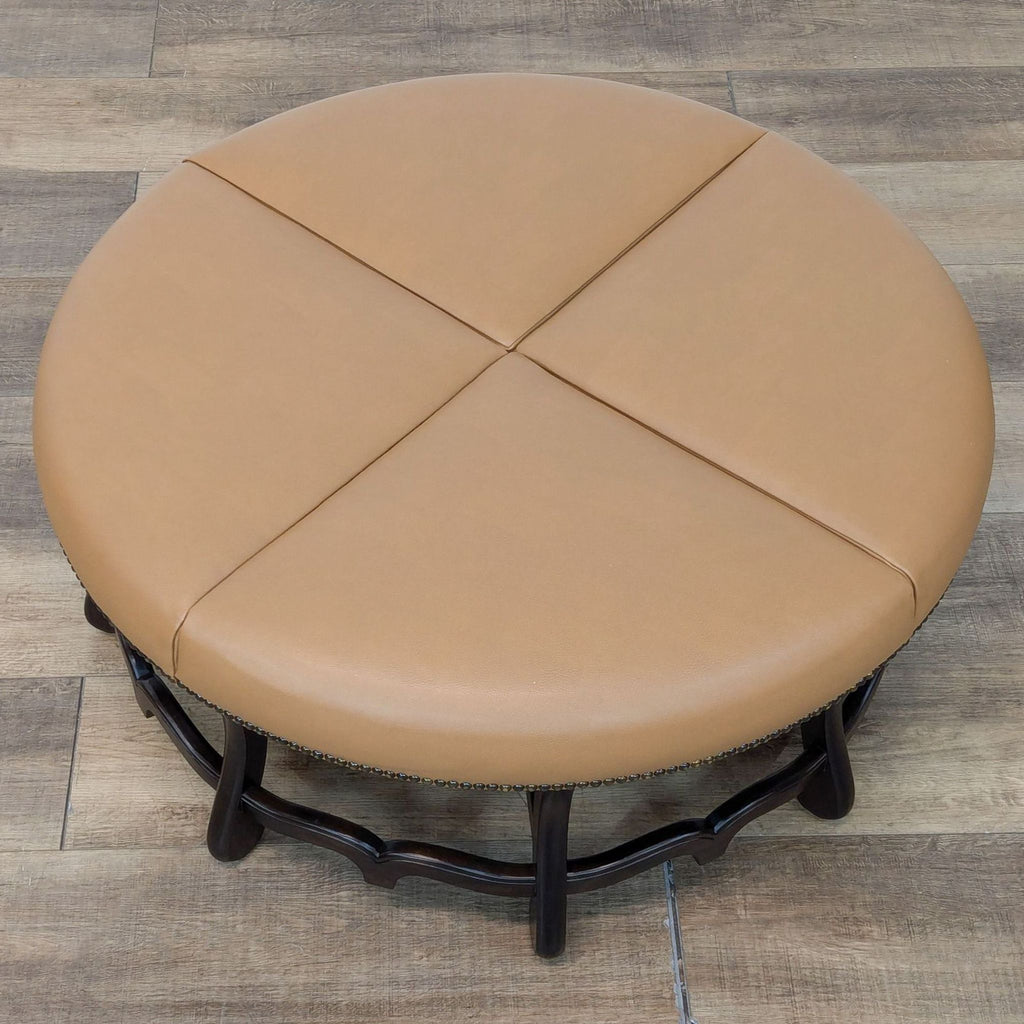 2. Overhead view of a circular tan leather ottoman divided into four sections, featuring ornate wooden legs.