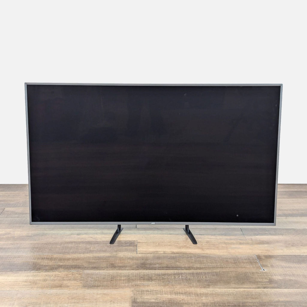 JVC TV front view on wooden floor, showcasing its sleek design.