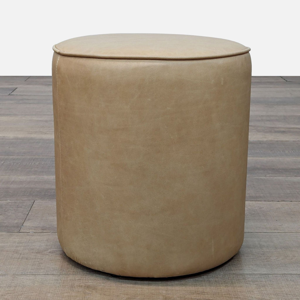 Round tan ottoman on a wooden floor.