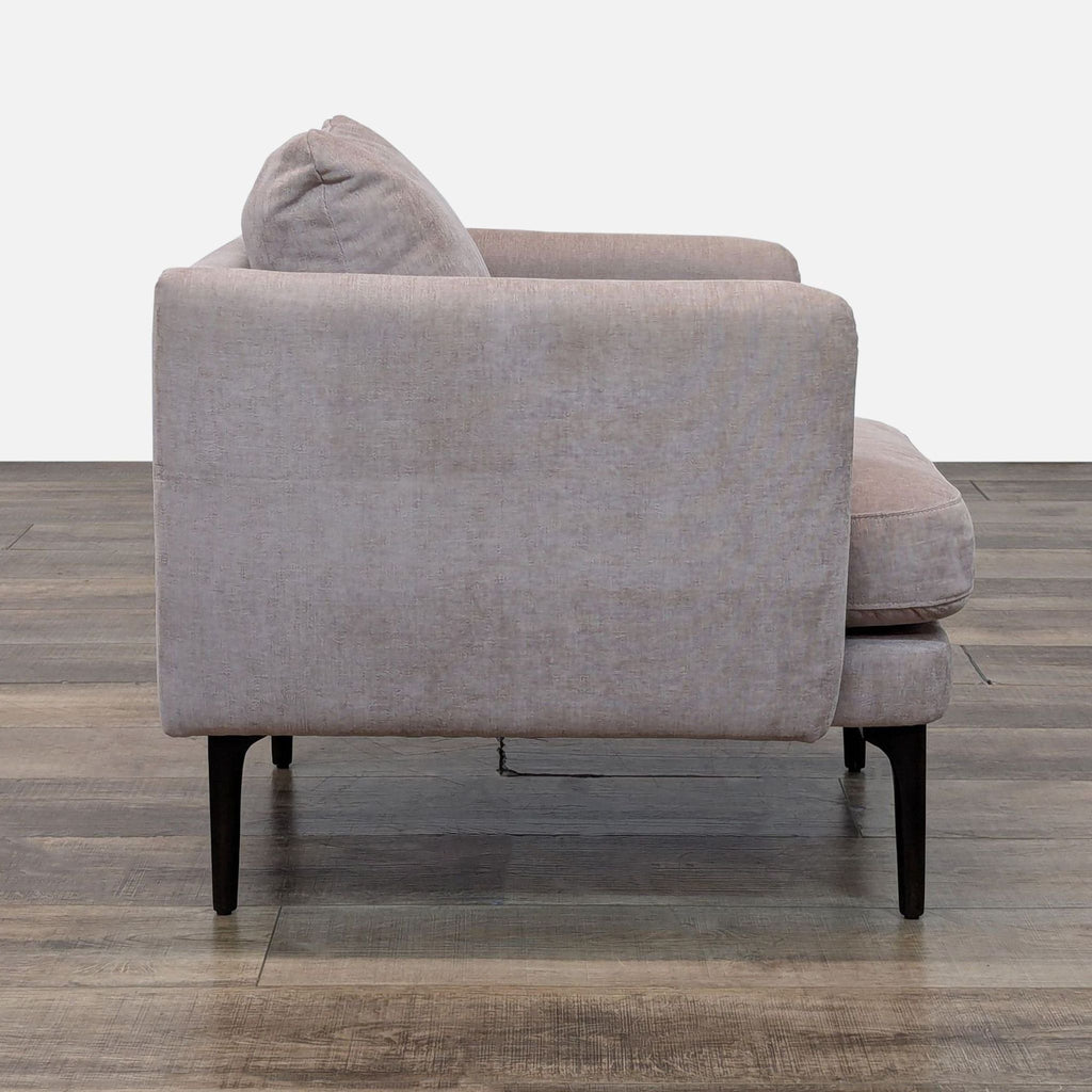 Side view of a beige West Elm lounge chair, showcasing its sleek wooden legs.