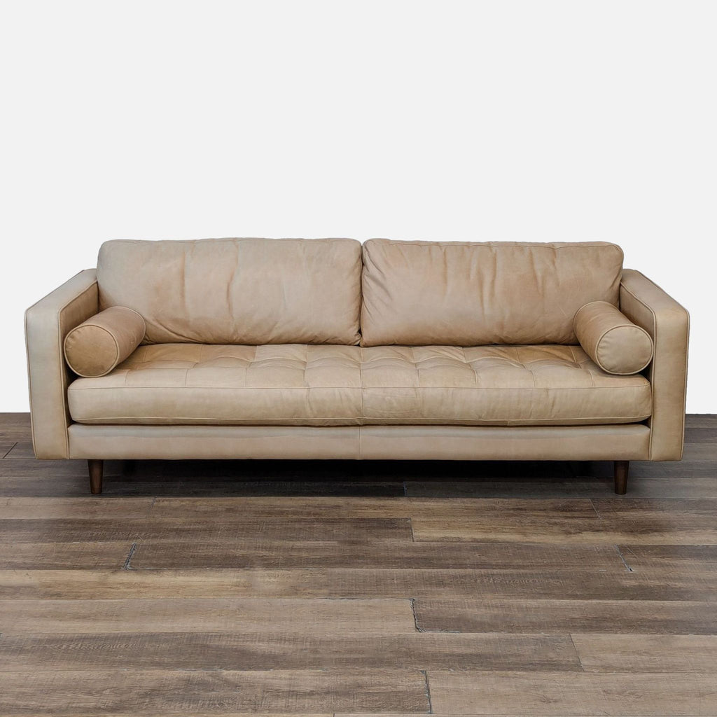 Front view of a West Elm 3-seat leather sofa with tufted seat and wood legs.