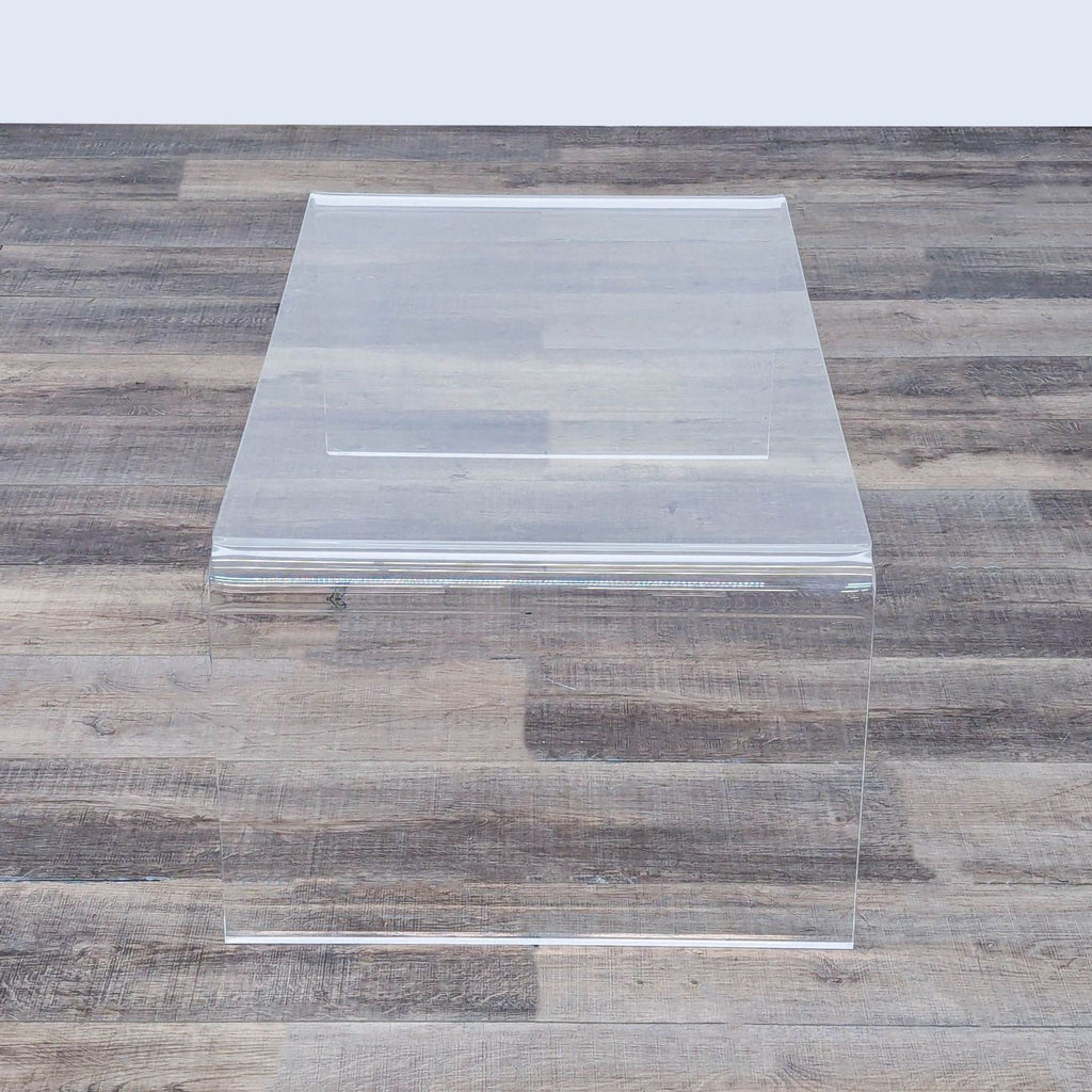 Modern acrylic coffee table, displaying a minimalist style against a wood-paneled floor.