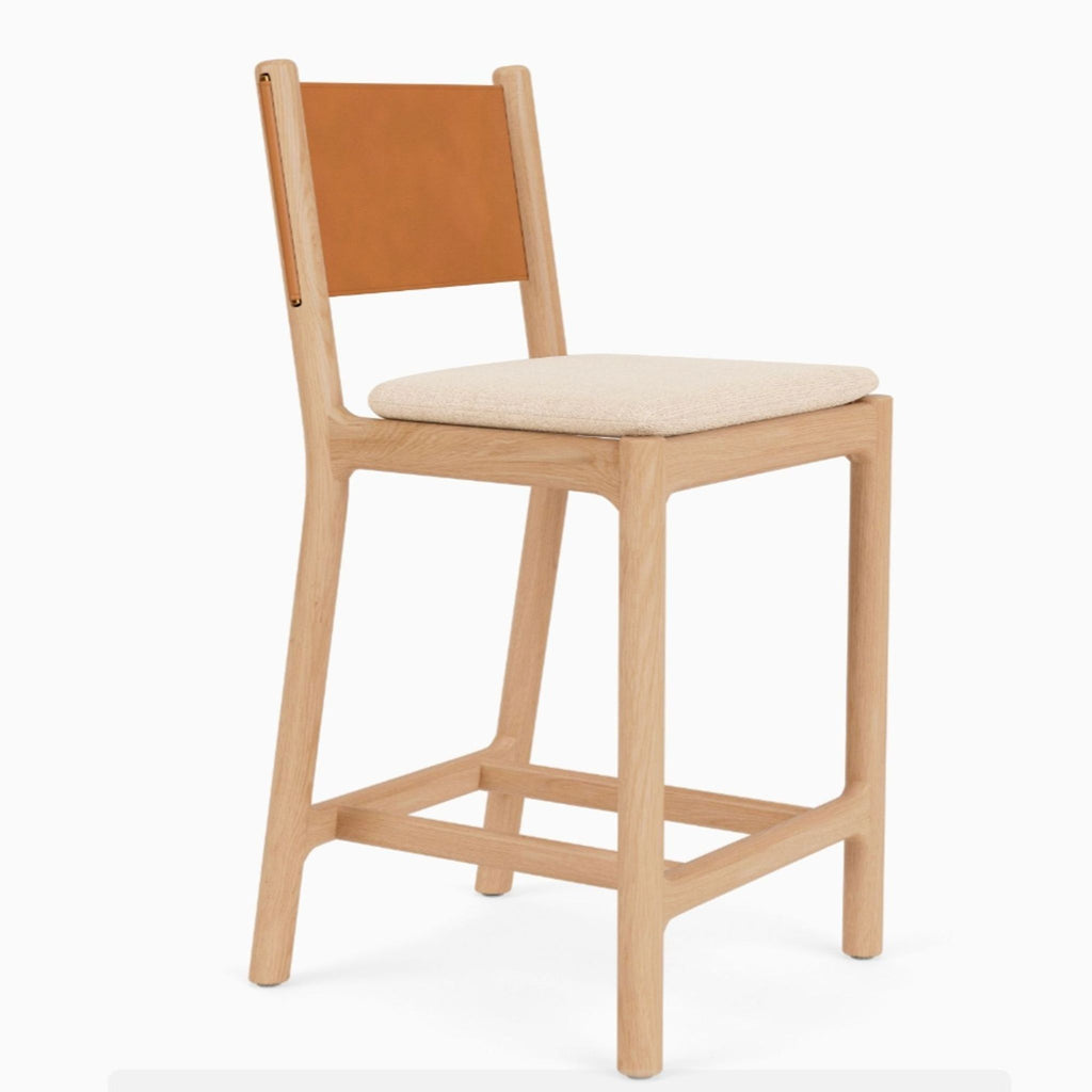 Italian leather seat back with visible brass pins and a removable woven cushion on a wooden stool by Denver Modern.  