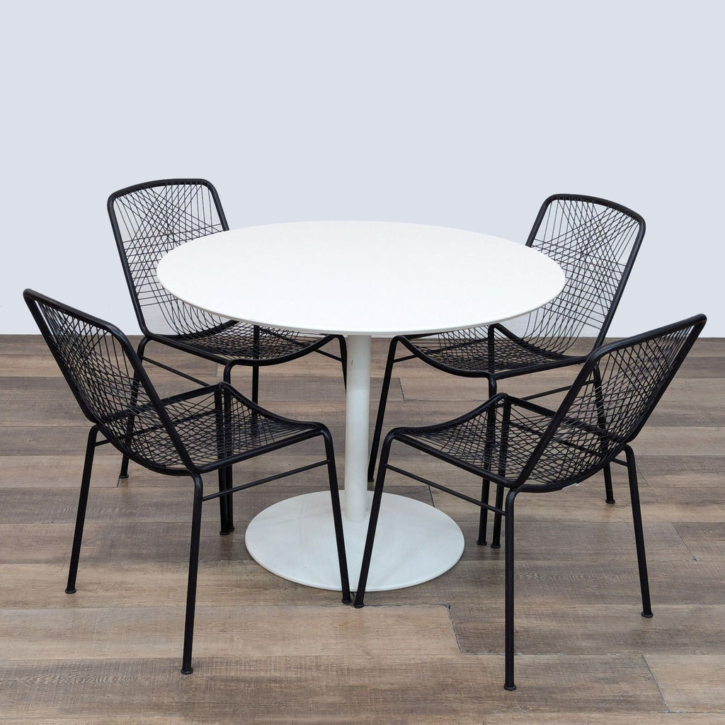 Round white dining table with four black woven-back chairs on wood floor.  