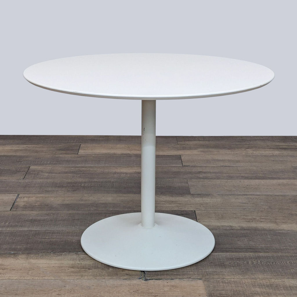 Minimalist white table with supportive base on wooden surface.  