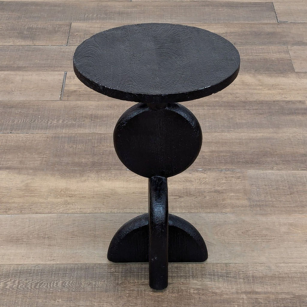 Tropical hardwood side table, rounded design with geometric base, on wood floor.