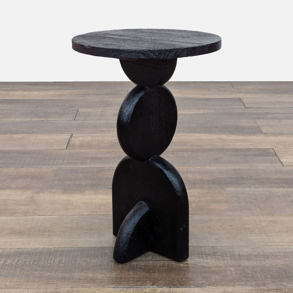 Handcrafted black round table with sculpted pillar base on wood floor.
