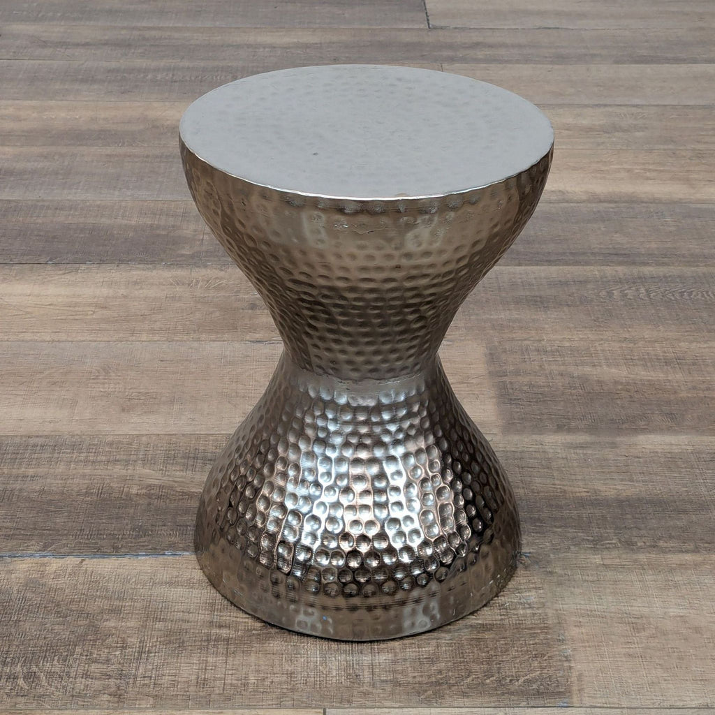 Textured silver console table, hourglass design, placed on wood surface.