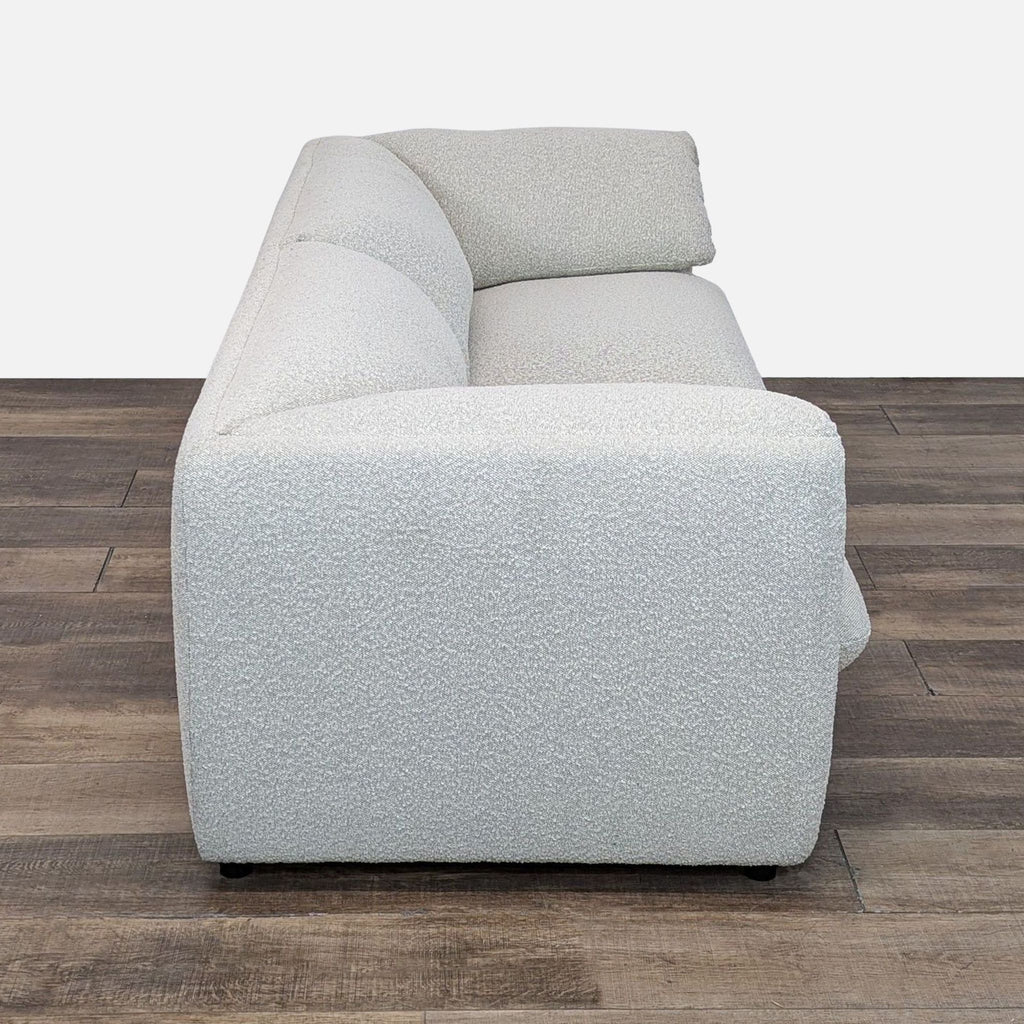 Side view of minimalist Lucas sofa, featuring white Bouclè upholstery, on a wooden floor.