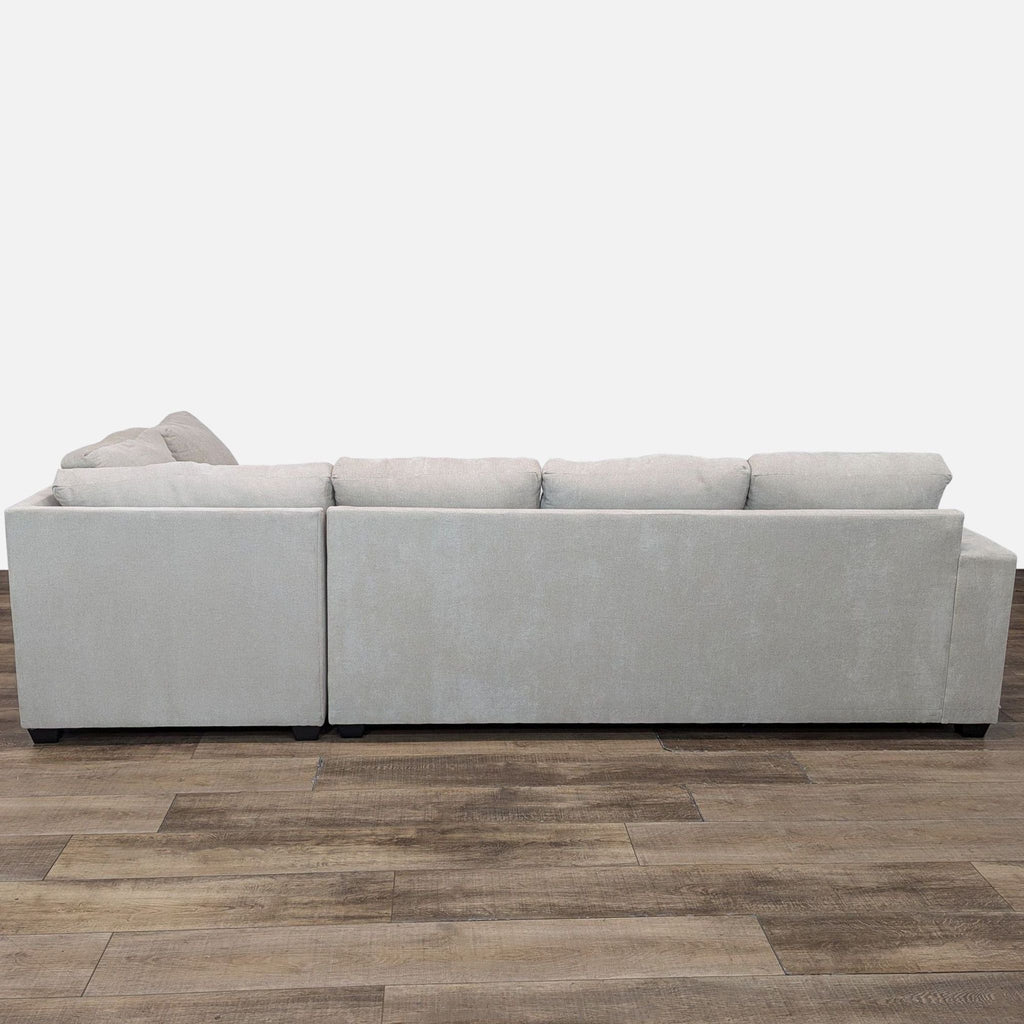 Back view of Living Spaces sectional, showcasing wide arms and cushioned design on wood floor.