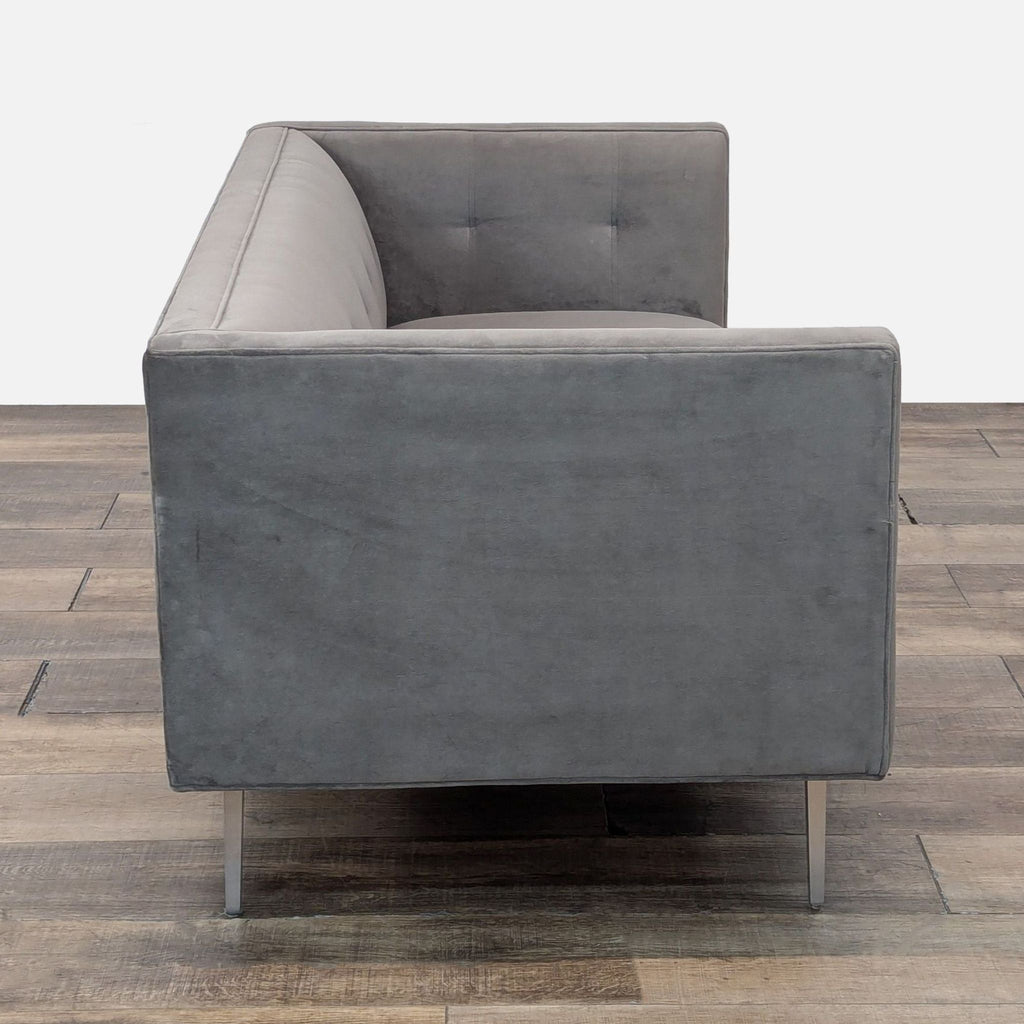 Side view of gray suede sofa with sleek metal legs, featuring button tufting.