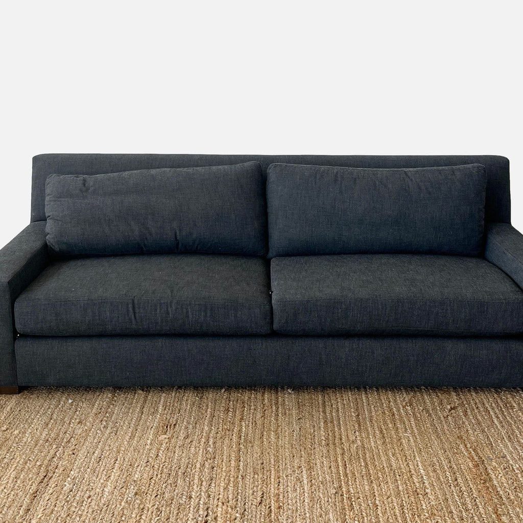 Sleek dark three-seat sofa by Reperch with track arms and loose cushions on a woven rug.