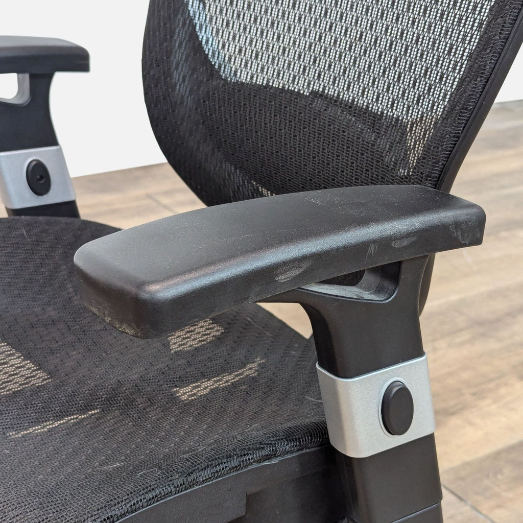 Close-up of a Staples chair's adjustable armrest and mesh back.