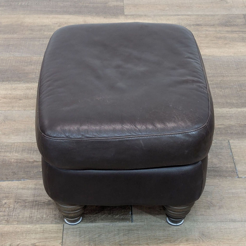 Lounge ottoman featuring rich brown leather and sturdy, turned wood legs, front view.