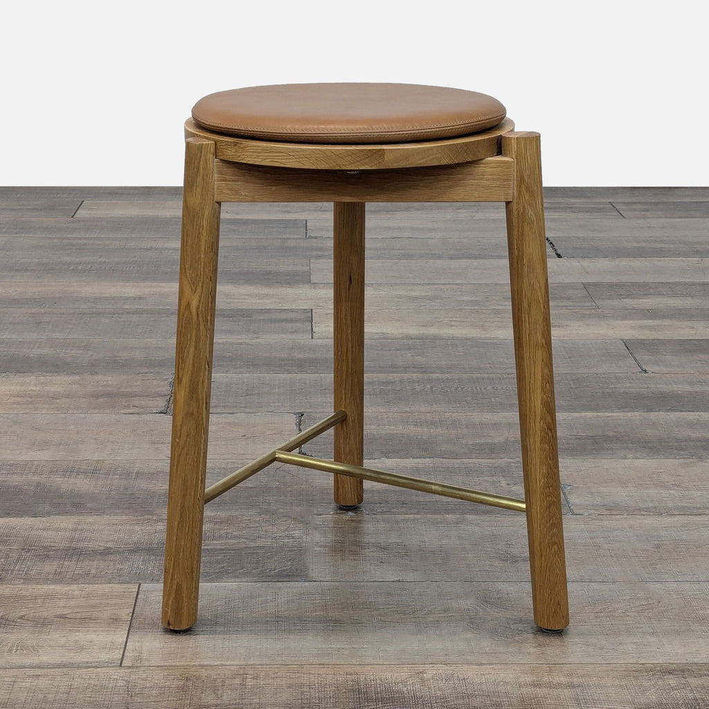 Wooden stool with a round leather seat and metal crossbar.