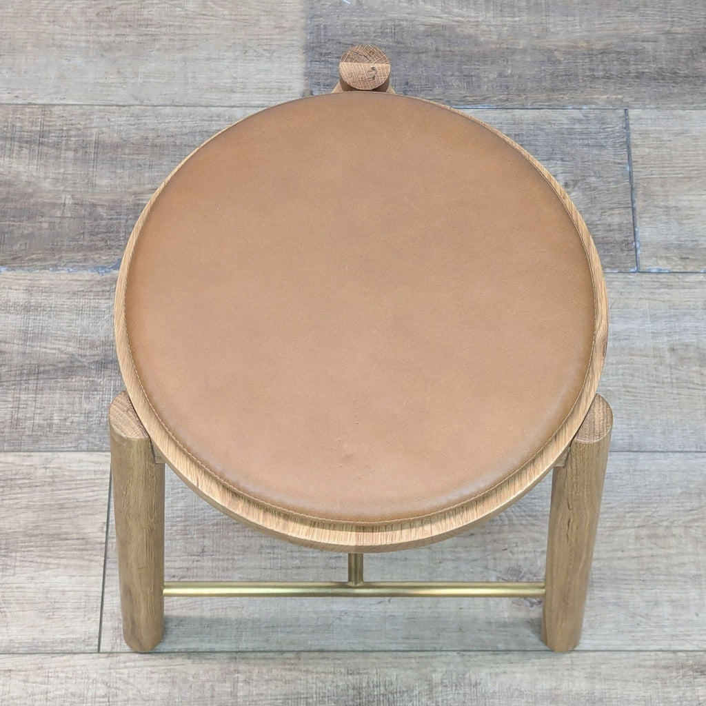 Side view of a minimalist stool with a tan leather seat.