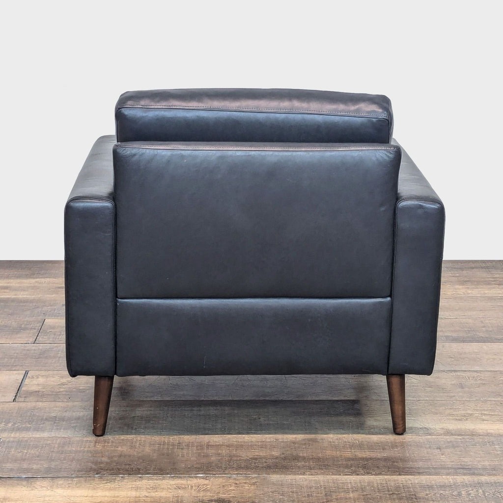 Back view of the Nomad lounge chair, highlighting black leather upholstery and wood legs.