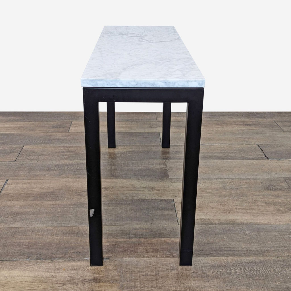 Narrow Crate & Barrel side table with marble top and black steel legs on wooden flooring.