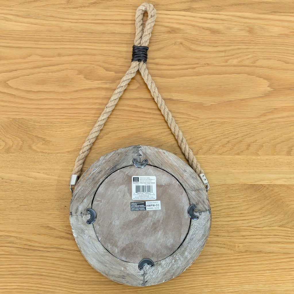 Back view of a rustic round mirror with rope loop and brand label on wooden surface. Brand: Heritage Home.