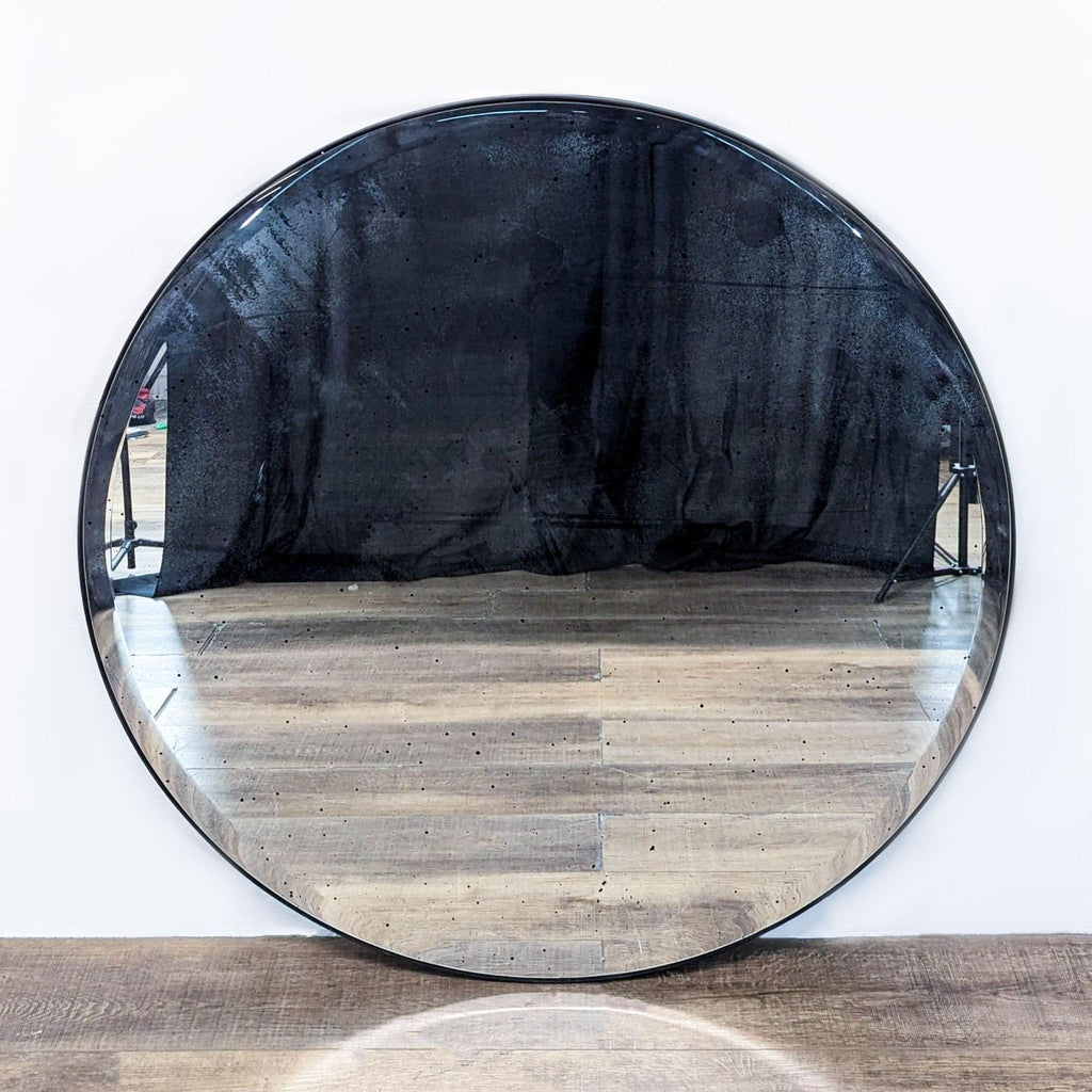 Round mirror with an antiqued finish, reflecting a wooden floor backdrop.  