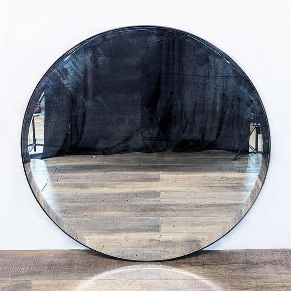 Round mirror with an antiqued finish, reflecting a wooden floor backdrop.  