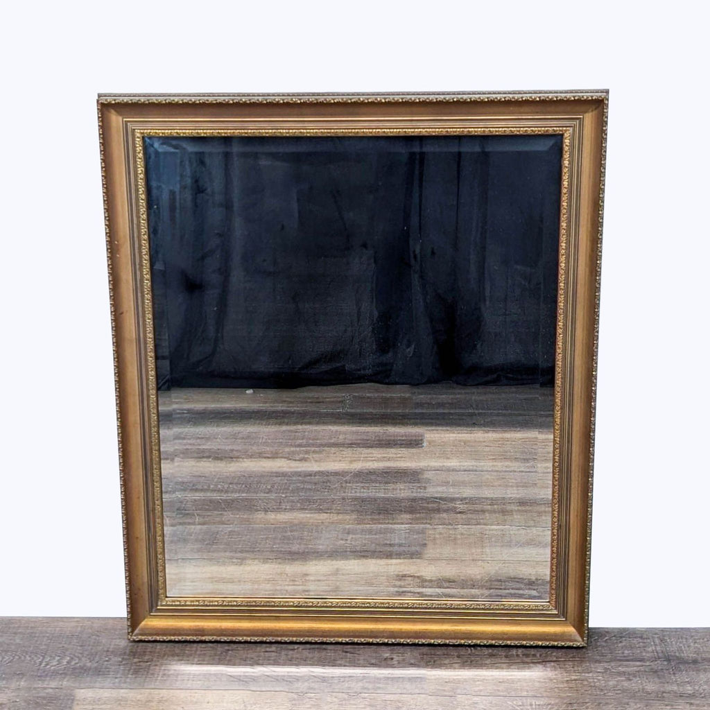 Square mirror with ornate, gold-toned frame by Reperch, on a wooden floor.