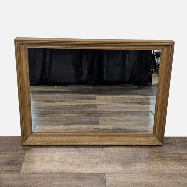 Reperch mirror with a wooden frame reflecting a wooden floor and black curtain backdrop.