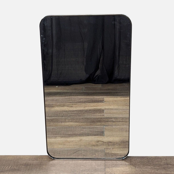 Rectangular mirror with rounded corners, reflecting a black drape and wooden floor.
