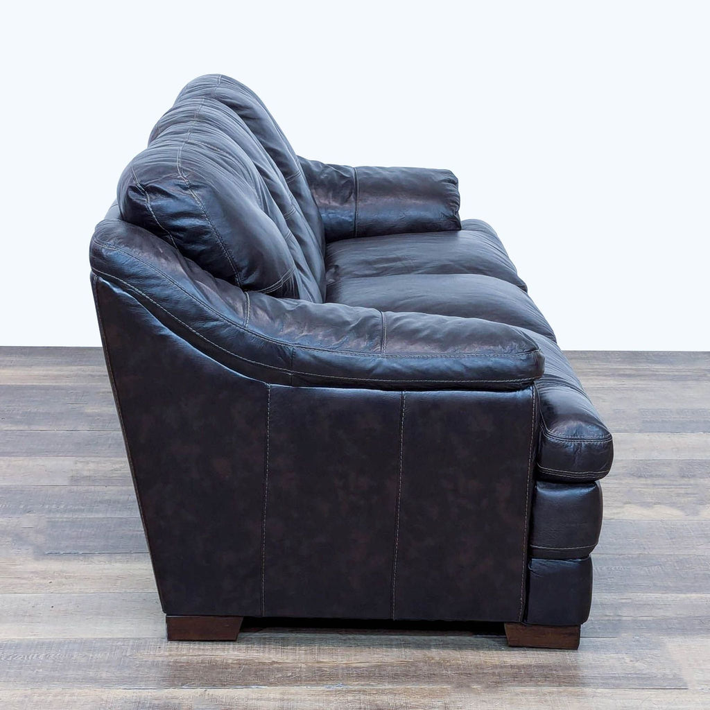 Side view of dark brown leather sofa featuring plush cushions, sloped arms, and button-tufted back.