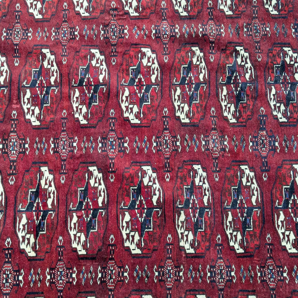 Close-up of the geometric Bukhara design on a hand-knotted Afghan rug in red tones.