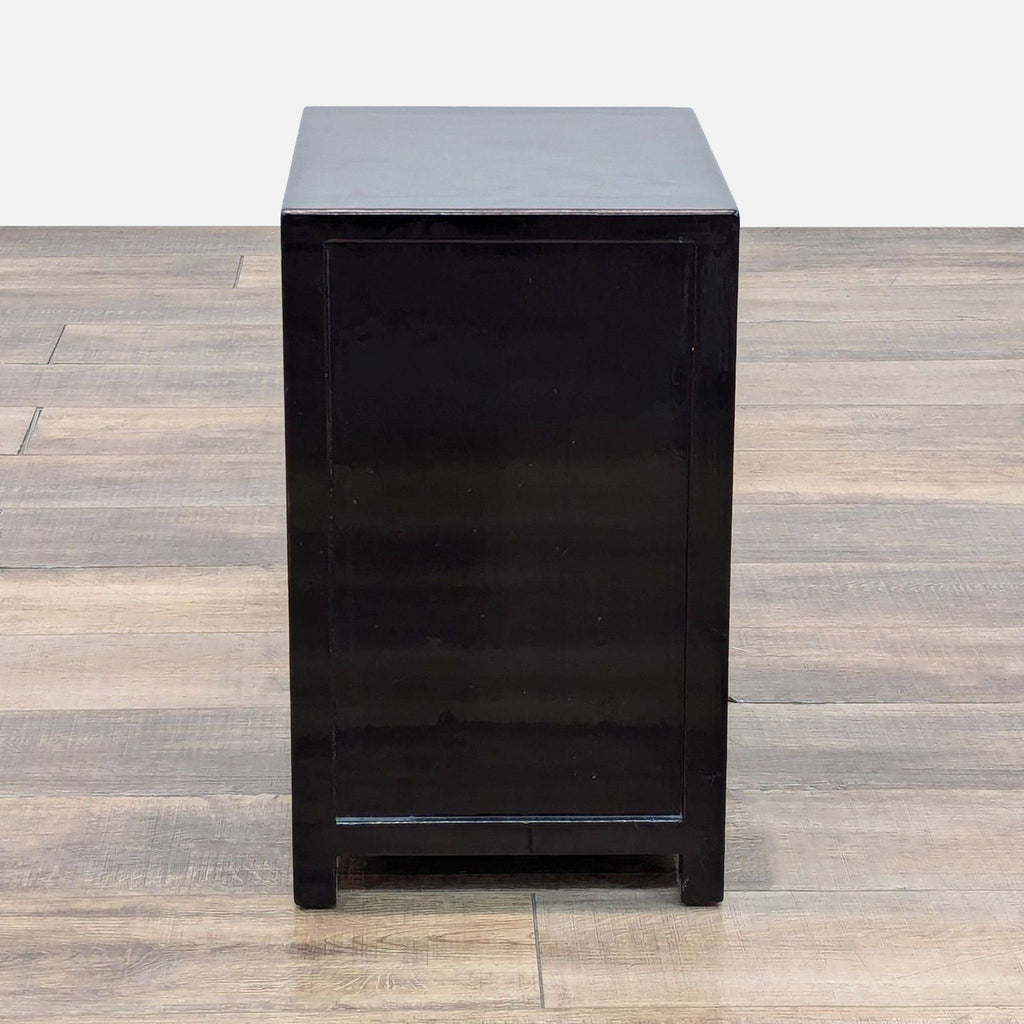 Side view of black wood nightstand on wooden floor.