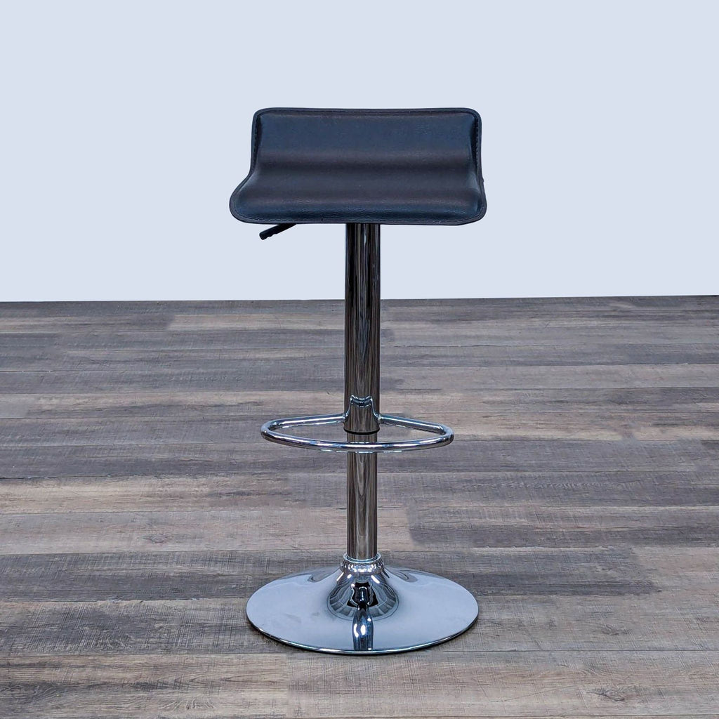 Black stool with faux leather seat, adjustable chrome pole, and footrest on wood floor.