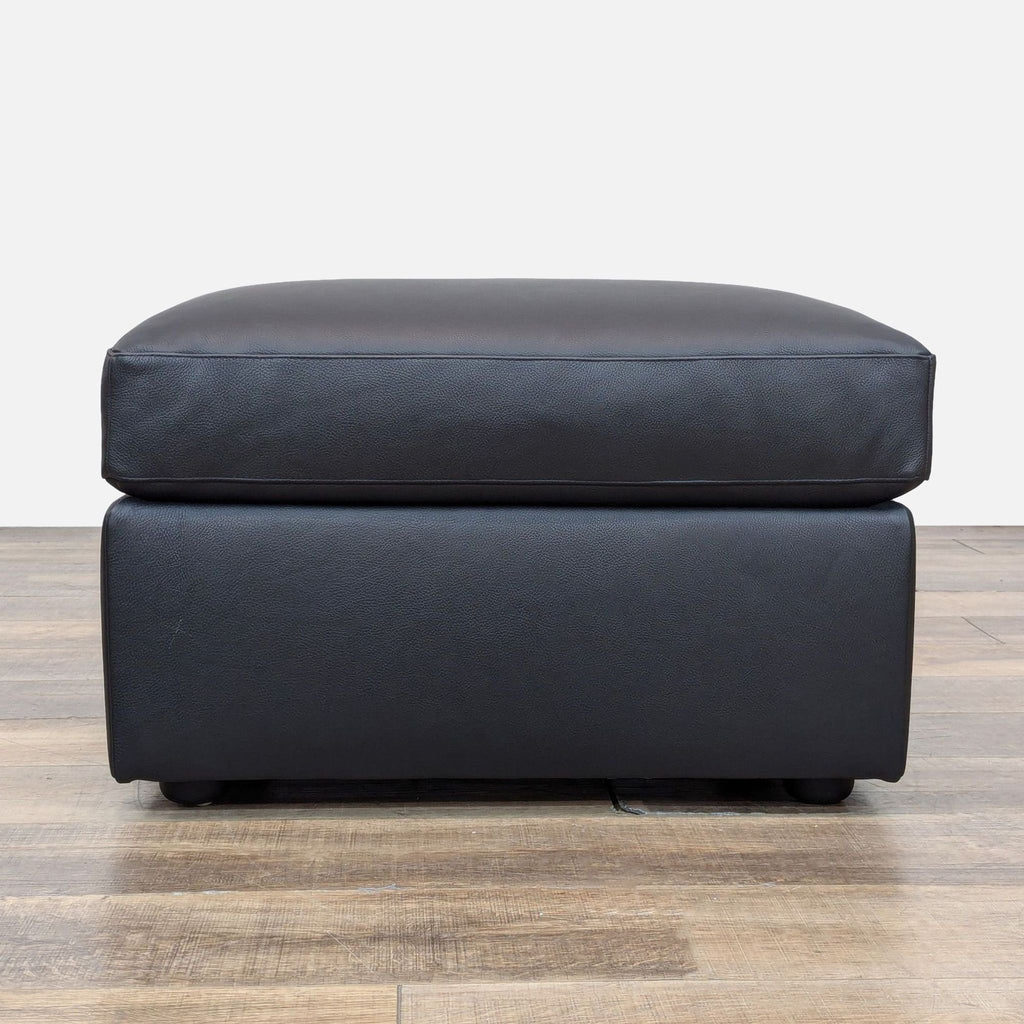 Side view of a black ottoman, minimalist design on wood flooring.