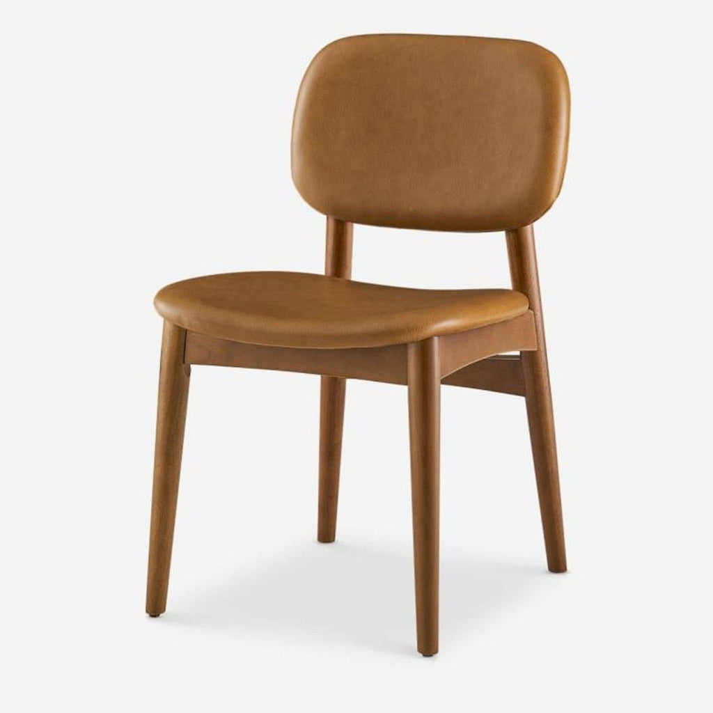 Angled view of a caramel leather dining chair with wood legs stained in walnut.