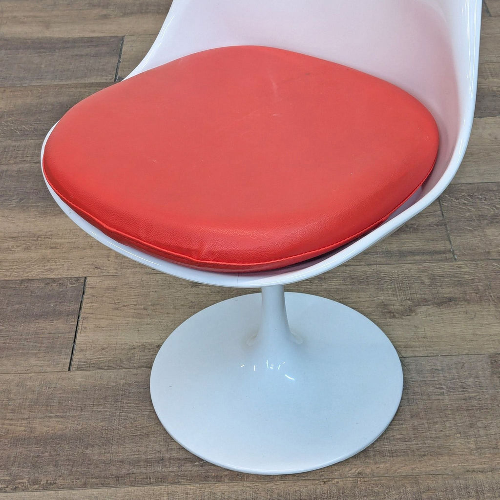 Close-up of red cushioned seat on white chair with round base.