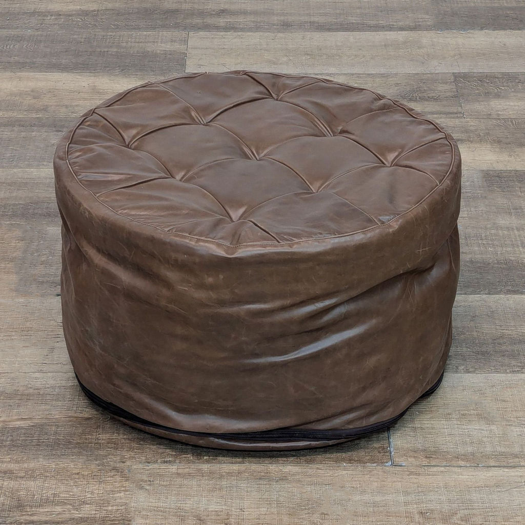 Round leather ottoman with removable slipcover on wood floor.