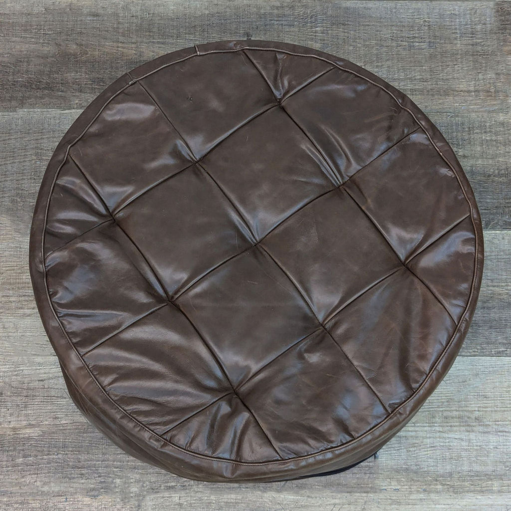 Top view of a quilted leather ottoman on wooden surface.