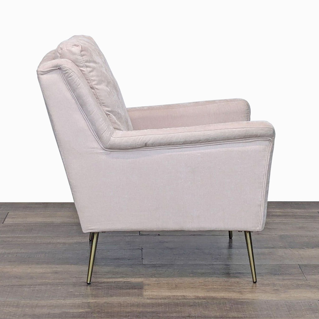 Side view of a pale pink velvet upholstered chair with gold legs.