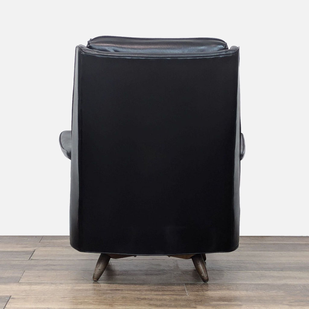 Back view of a Reperch black leather lounge chair highlighting smooth leather and wooden legs.  