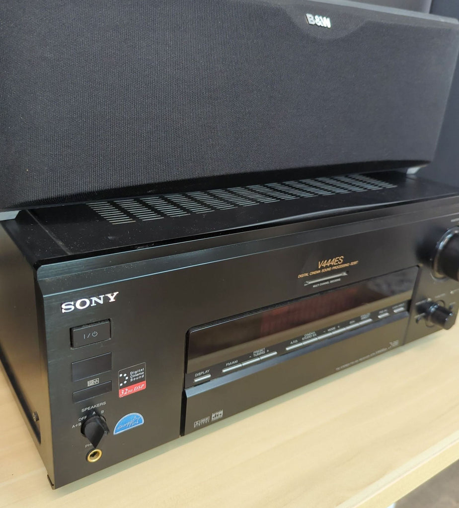 Close-up of a Sony amplifier below a B&W center speaker, highlighting control buttons and logo.