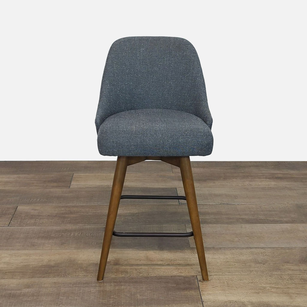 Front view of a gray upholstered stool with wood legs and metal footrest.