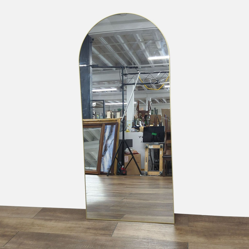 Arched floor mirror with a gold frame by Reperch in an industrial setting.
