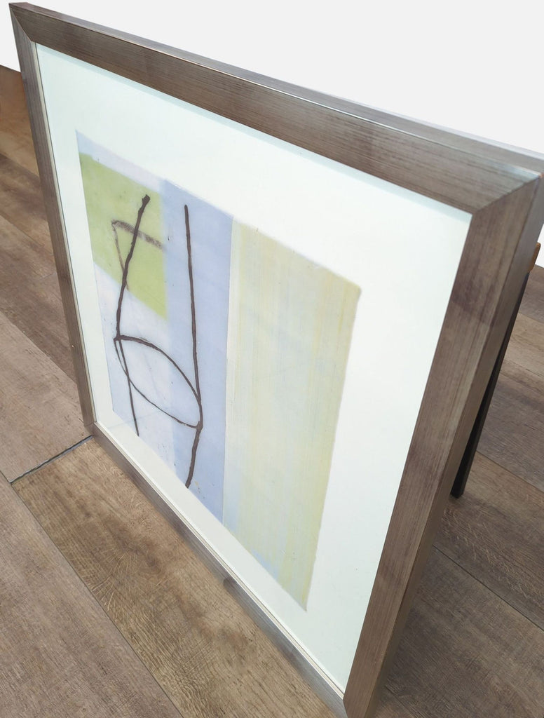 Side view of abstract art in a silver frame, placed on a wooden surface.