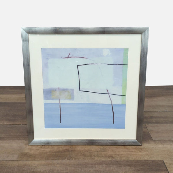 Abstract print of lines and squares in a silver frame on wooden floor.