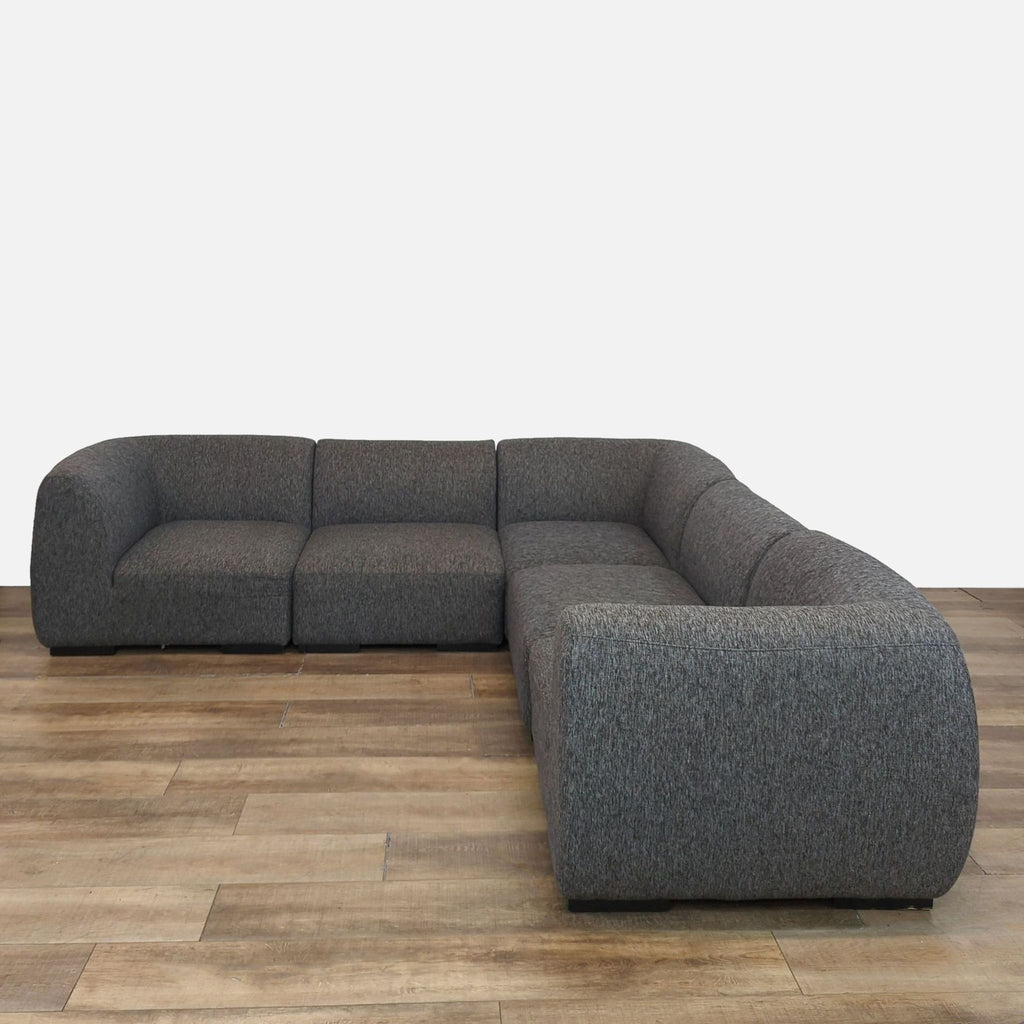 Gray modular sectional with tailored upholstery and wood feet on a wooden floor.