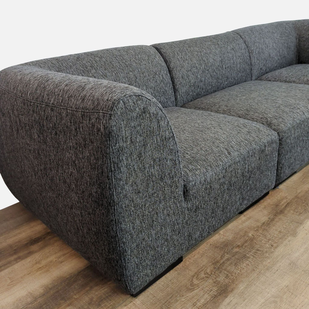 Close-up of gray sectional with soft upholstery and curved armrest, Reperch brand.