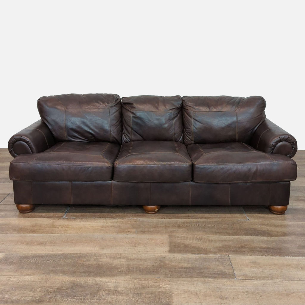 Traditional leather sofa with plush cushions, wood feet, and rolled arms by Reperch.